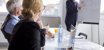 businesspeople-looking-man-giving-presentation-flip-chart