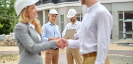Man and a woman in protective helmets greeting each other in the presence of construction workers