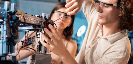 Young man and woman in protective glasses doing experiments in robotics in a laboratory. Robot on the table